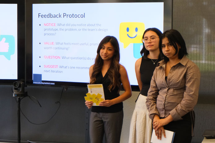 Three UC Davis students stand in front of a presentation screen during a Courage Museum internship project showcase.